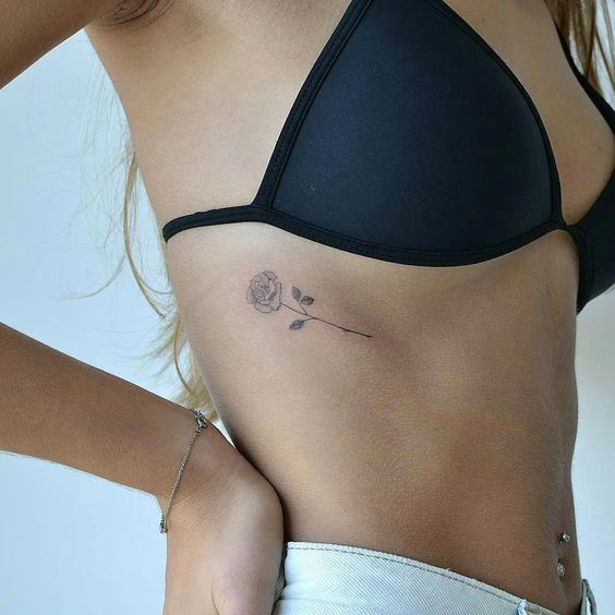 Girl with a small and minimalist upper ribcage tattoo of a rose