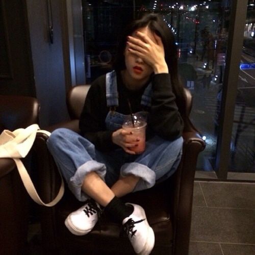 Girl wearing overalls and face-palming while holding a drink