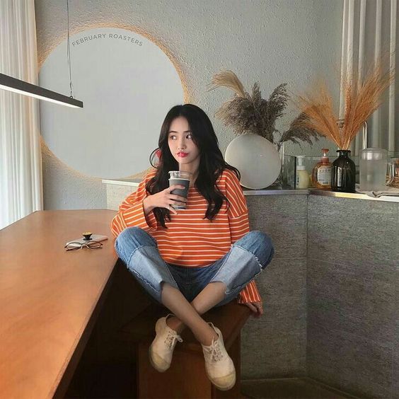 korean girl wearing orange top and jeans while taking a sip of her drink