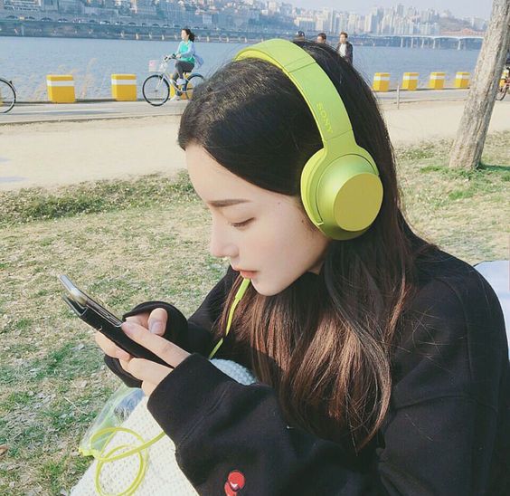 korean girl wearing green headphones and looking at her phone while at the pier