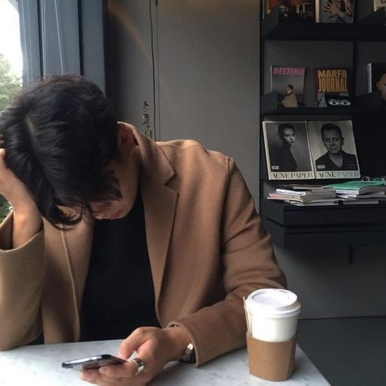 asian guy wearing a brown coat and looking at his phone