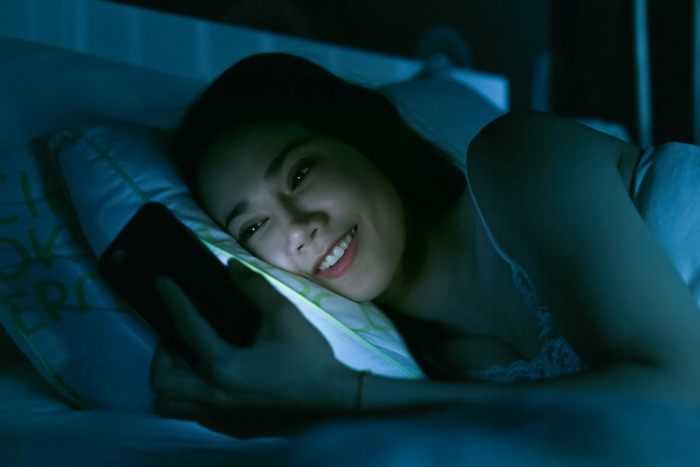 Girl laying on bed using phone in the dark