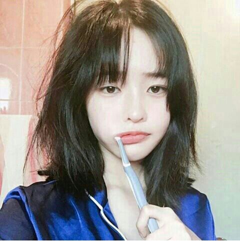 Asian girl with short hair and bangs brushing her teeth