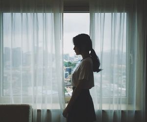 Korean woman standing in front of a window with sheer day curtains
