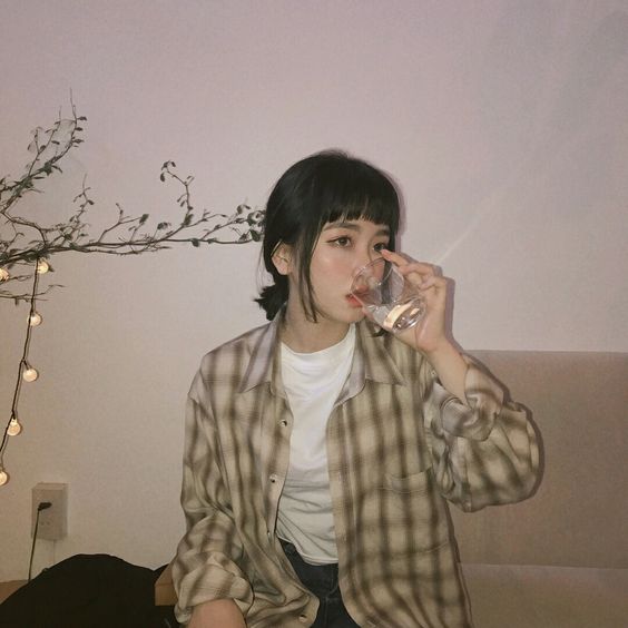 asian woman with glasses and a checkered shirt drinking a glass of water