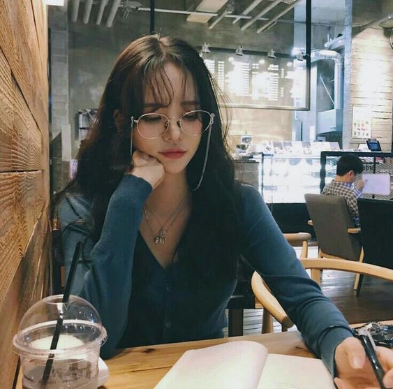 asian woman wearing glasses and reading a book with her hand on her chin