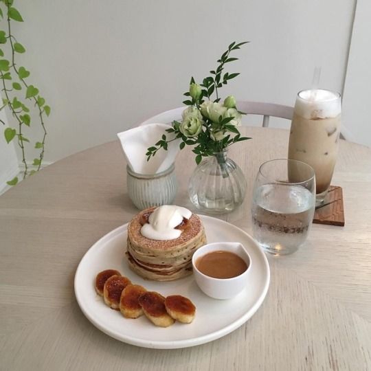 korean cafe with round wooden table, pancakes, coffee and small vase of flowers