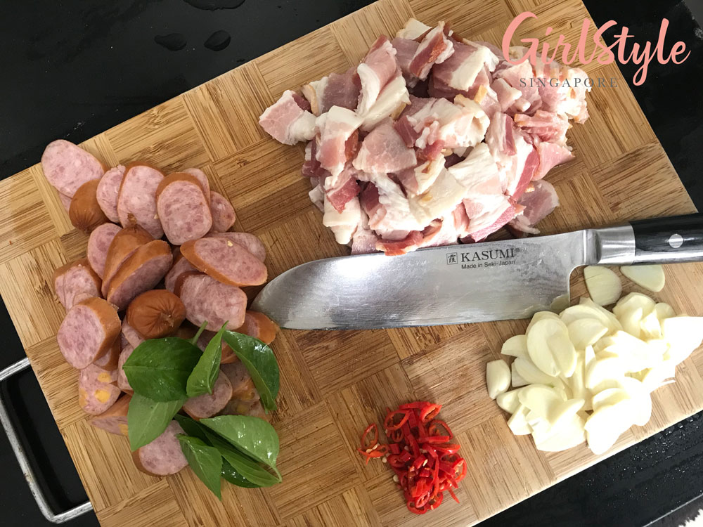 chopping board with knife and ingredients for bacon aglio olio pasta with sausages