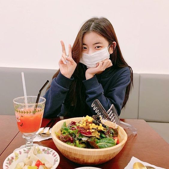 korean girl eating a salad and wearing a white face mask