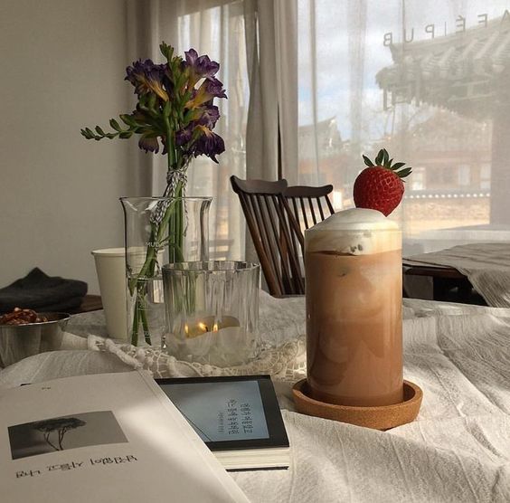 iced coffee with a strawberry on top and a vase of flowers on a table