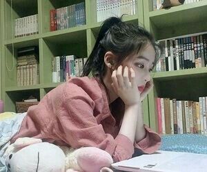 asian girl wearing pink top with hands on chin in library