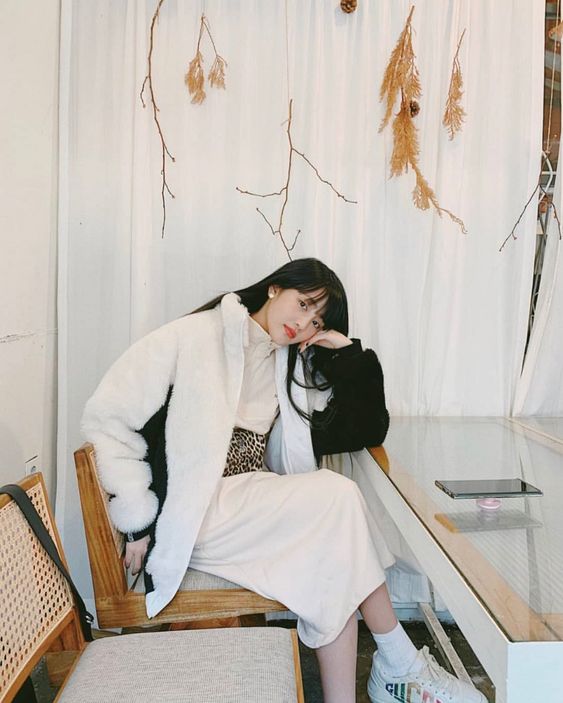 asian woman wearing all white sitting with hand on cheek