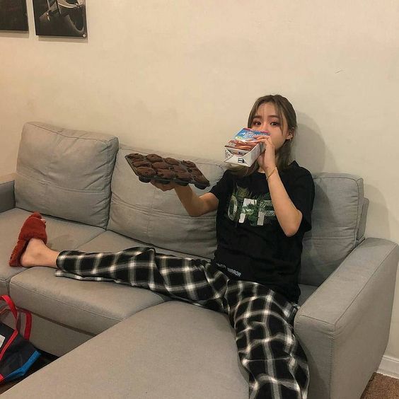 asian woman sitting on the sofa eating cupcakes and drinking milk