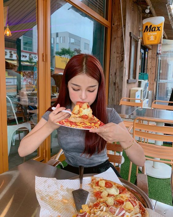 asian girl eating a slice of pizza