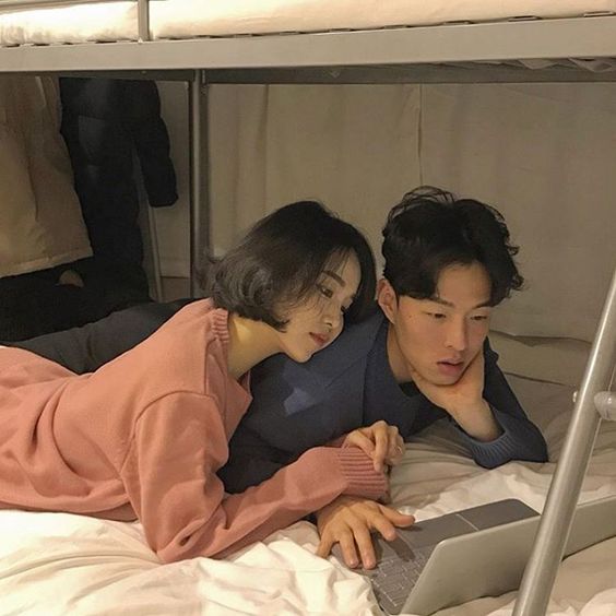 asian couple lying on bed and watching shows on a laptop