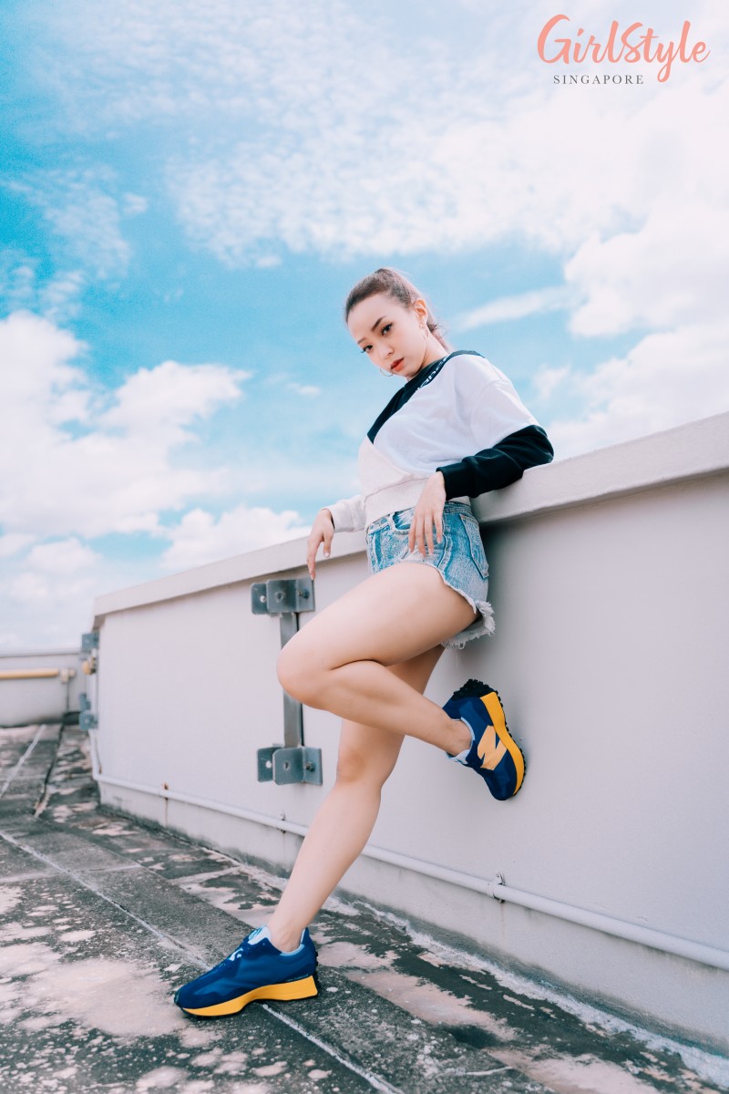 asian girl wearing New Balance 327 sneakers in blue, denim shorts and oversized Athletics Village Crew