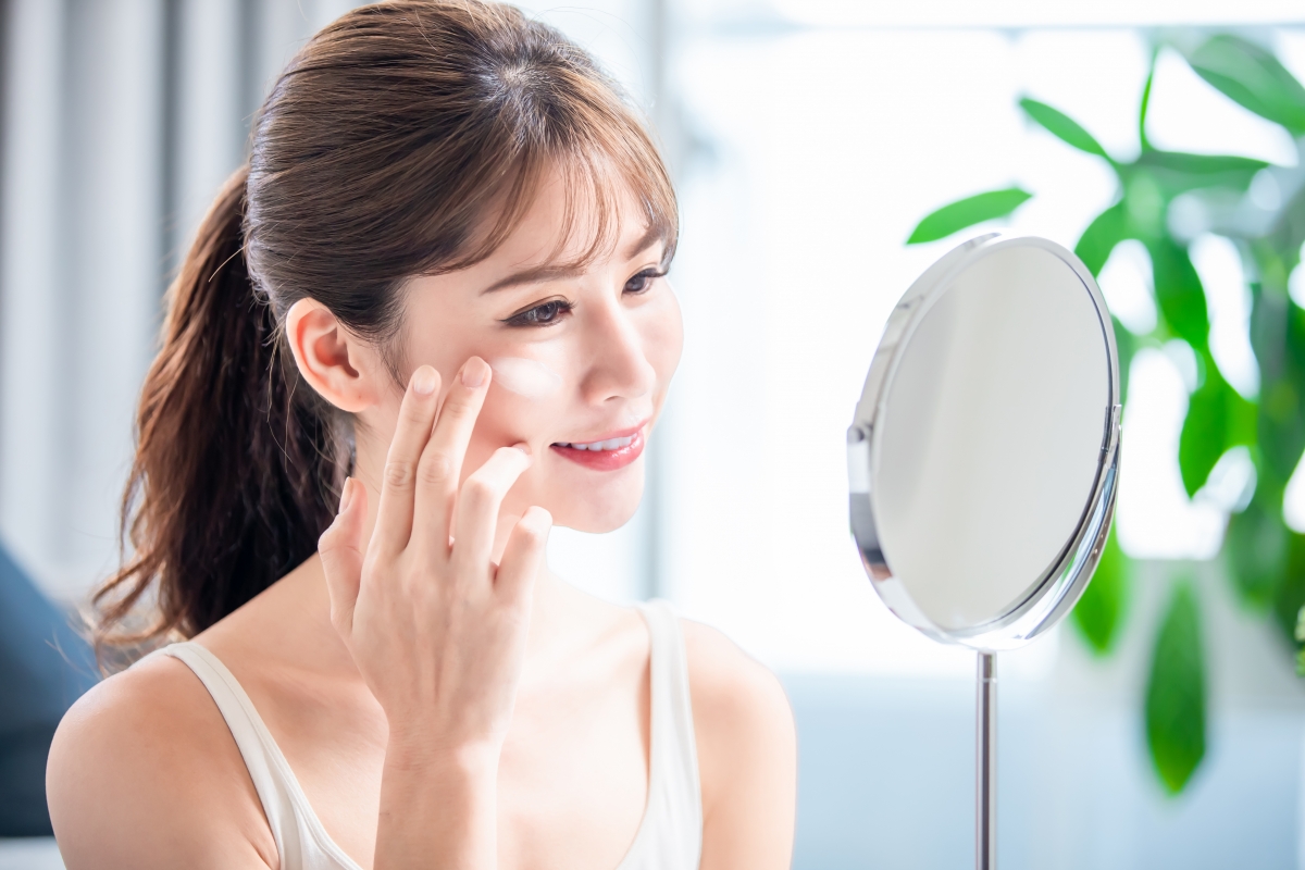 Girl applying sunscreen indoors in front of a table mirror