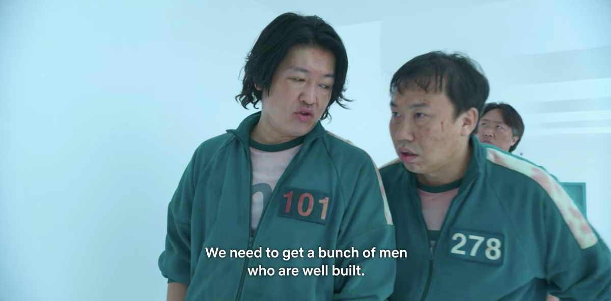 Deok su asking his men to gather male players for the tug-of-war challenge in squid game