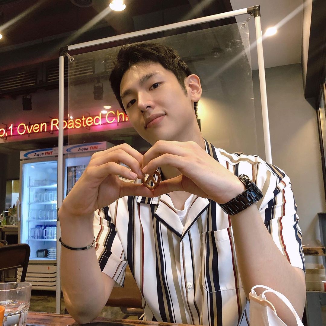squid game lee jong jun korean actor in a cafe wearing striped shirt playing the square mask manager guard in pink jumpsuit